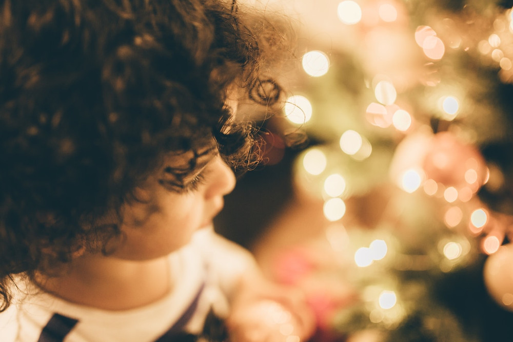 a small girl looks at tree lights