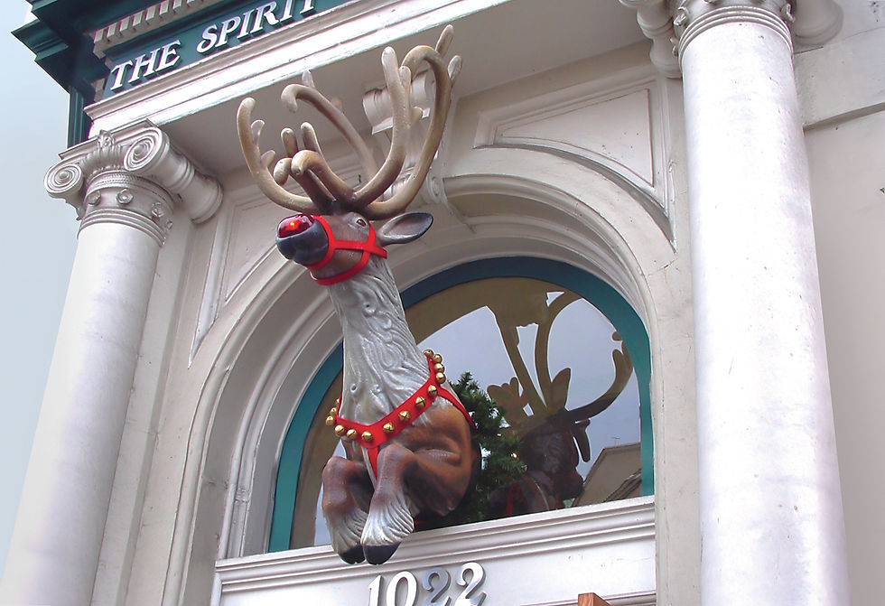 A festive reindeer sculpture mounted above the entrance of a building, with antlers decorated in red harness and bells, creating a welcoming holiday atmosphere.