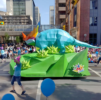 Royal Tyrrell Museum Parade Float: A vibrant geometric triceratops parade float with bright colors representing the Royal Tyrrell Museum, parading in front of a large crowd.