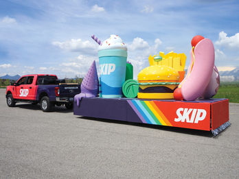 Skip the Dishes Float: A colorful parade float featuring giant sculptures of a milkshake with sprinkles, ice cream cone, burger, fries, and a hot dog, all branded with the "Skip the Dishes" logo. The sculptures are vibrant, giving a playful and eye-catching effect.