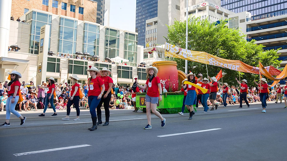 A bright and creative float for the University of Calgary, showcasing a giant jar labeled “Dreams” filled with colorful stars and floral decorations. Marchers in red shirts walk alongside with vibrant banners.