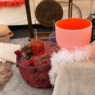 inside a white dome tent. table with one glass singing bowl and a white feather boa. a gong on a stand in the background