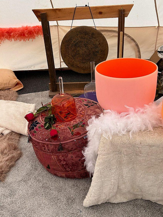 inside a white dome tent. table with one glass singing bowl and a white feather boa. a gong on a stand in the background