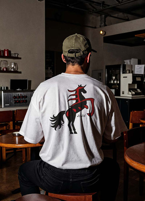 Mockup d'un homme assis de dos dans un café portant un t-shirt blanc avec un dessin de cheval noir entrelacé du signe rouge chinois du cheval