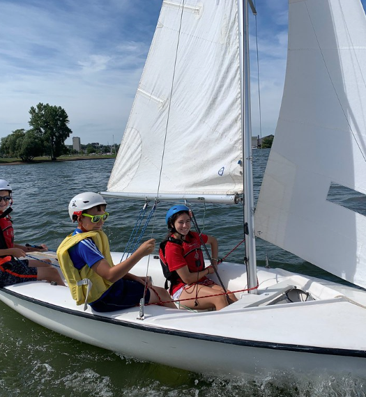 Three students sailing a small boat on a lake