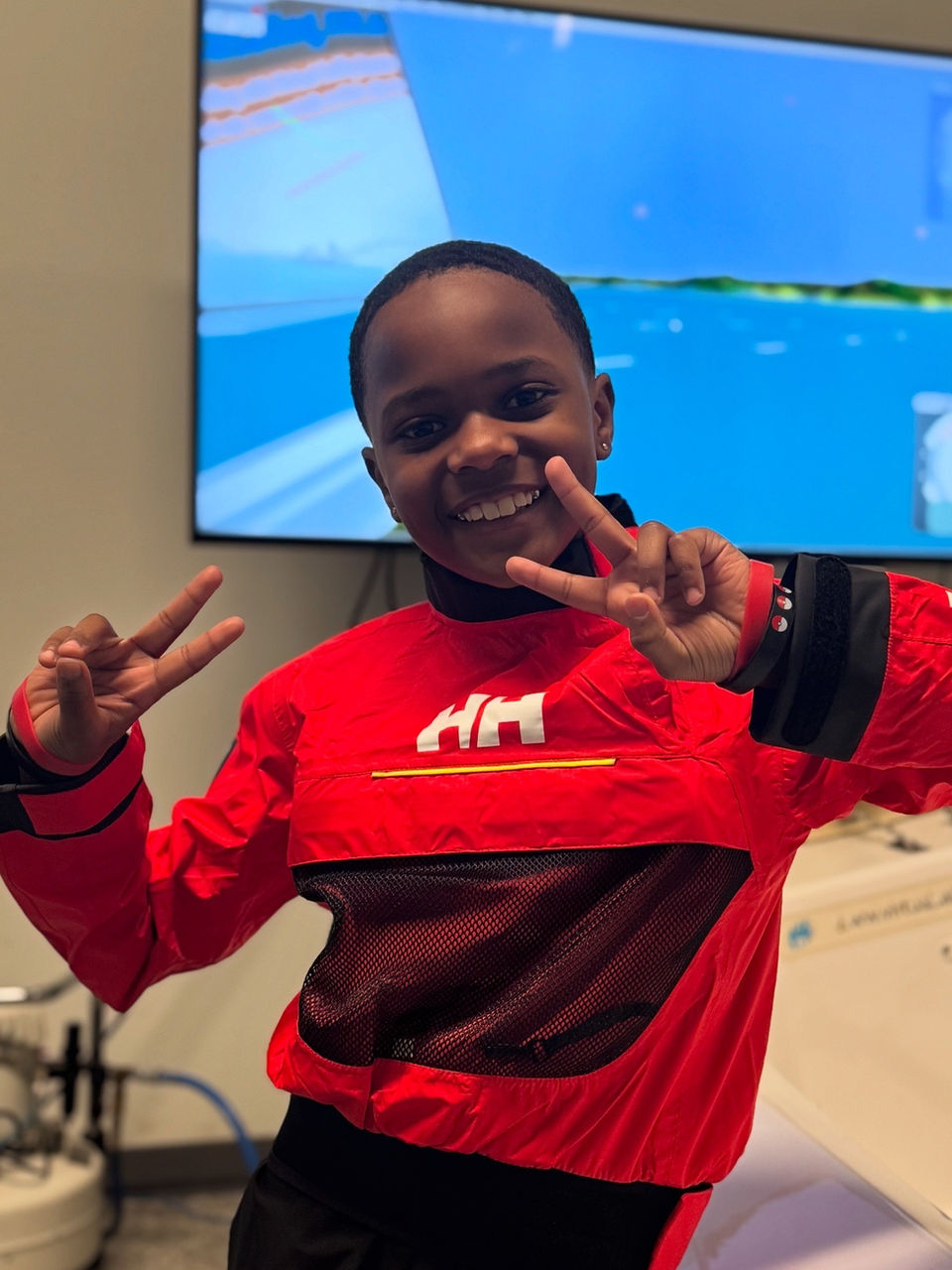 Smiling child making peace signs in front of a sailing simulator screen