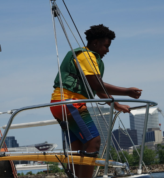 Young person on a sailboat with a city skyline in the background.