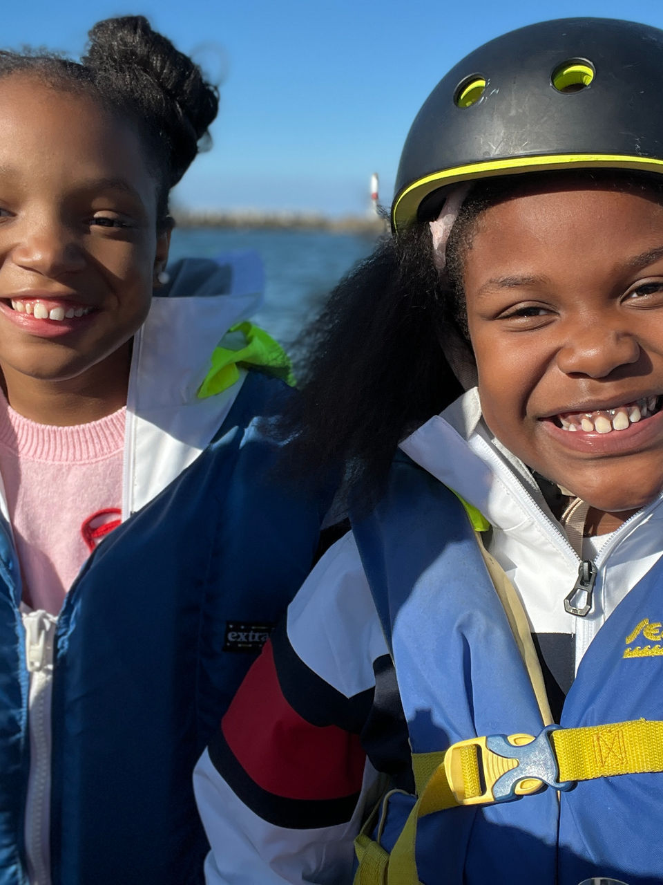 Two smiling children, one wearing a life vest and helmet