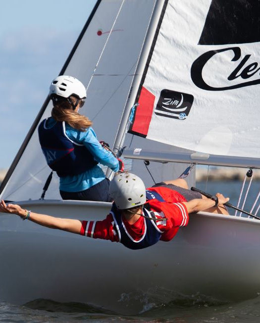 Two sailors on a small boat, one hiking out, 'Cleveland' on sail