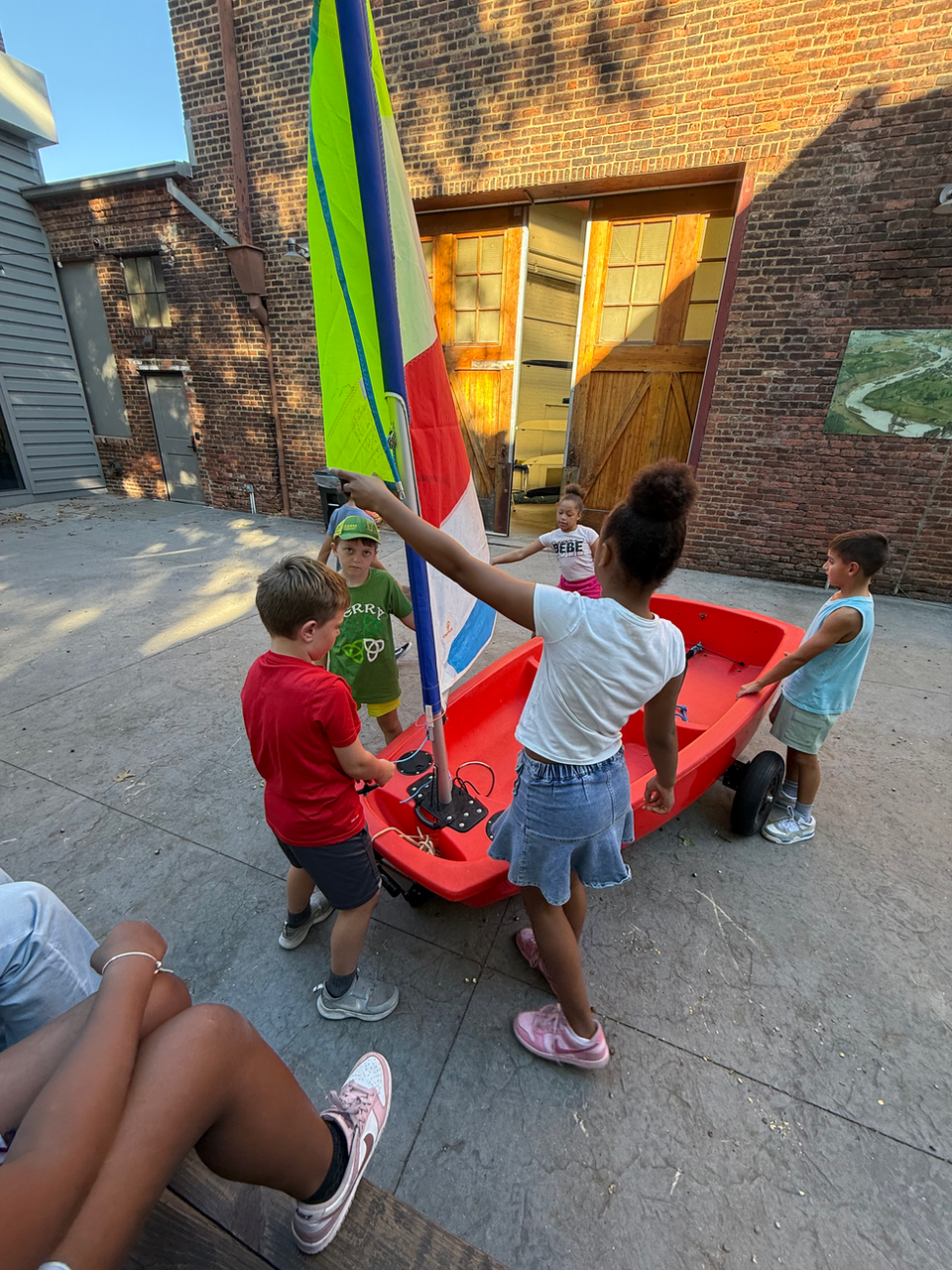 Kids playing with a small red sailboat with a colorful sail