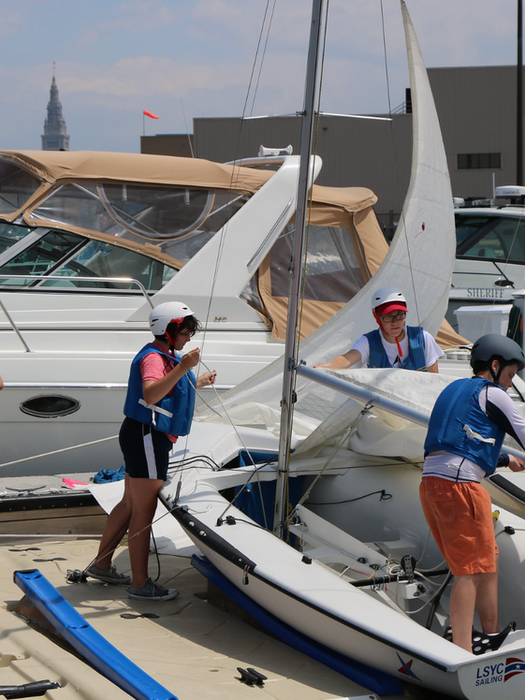 Children preparing small sailboats at a dock for sailing camp.
