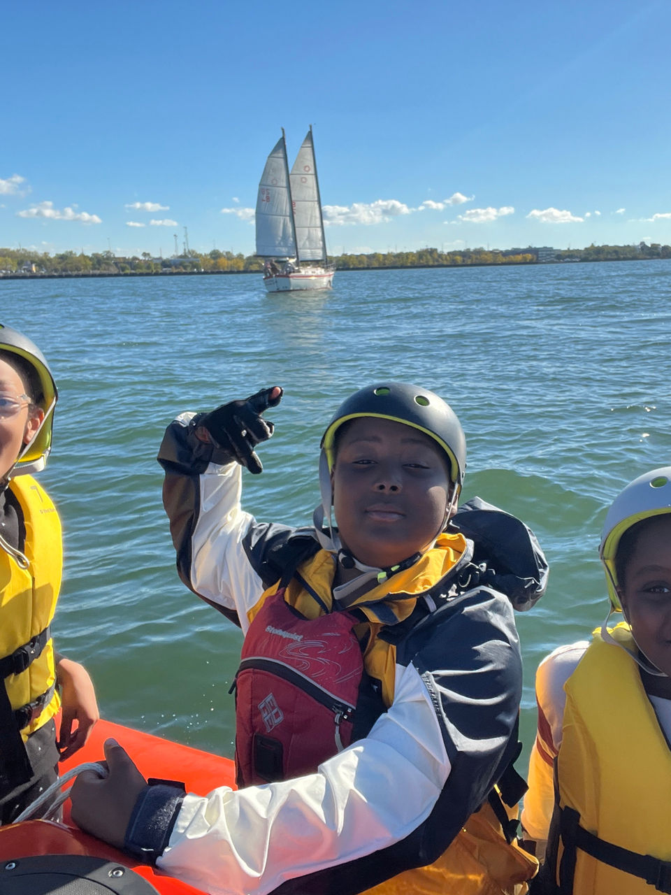 Smiling children in life jackets on a boat, sailboat in background