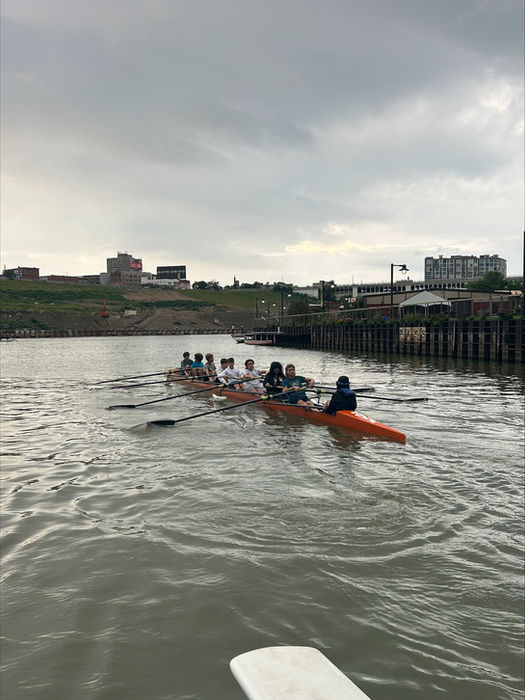 Rowing team practices on river with buildings ashore
