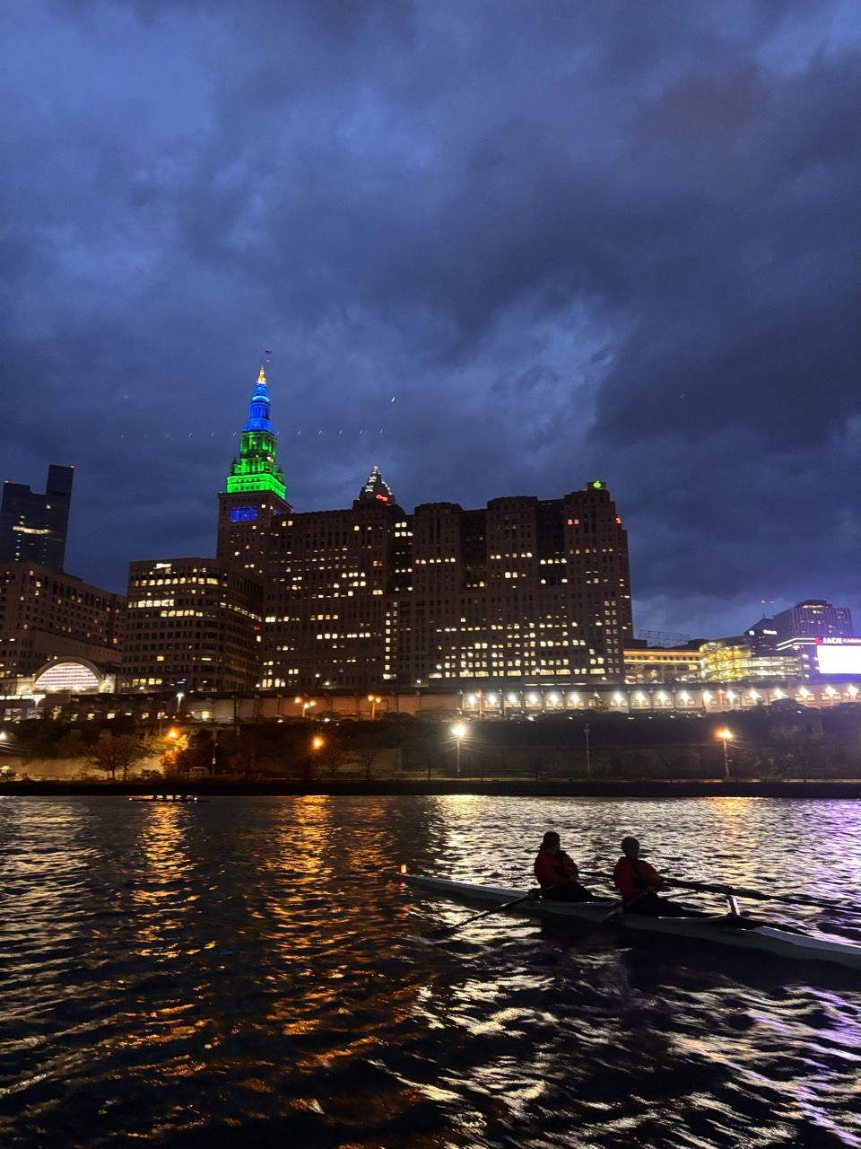 Two rowers on water at night with illuminated city skyline