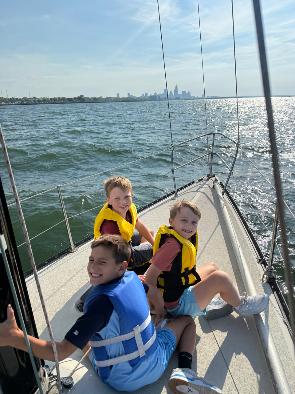 Three boys in life vests on a sailboat with city skyline