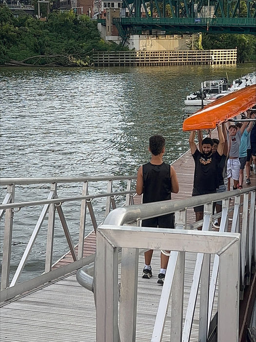People on a dock by a river with a green bridge