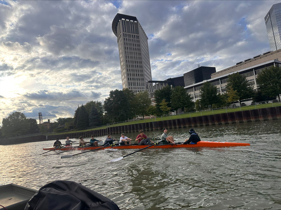 Crew team rowing on a river with city buildings