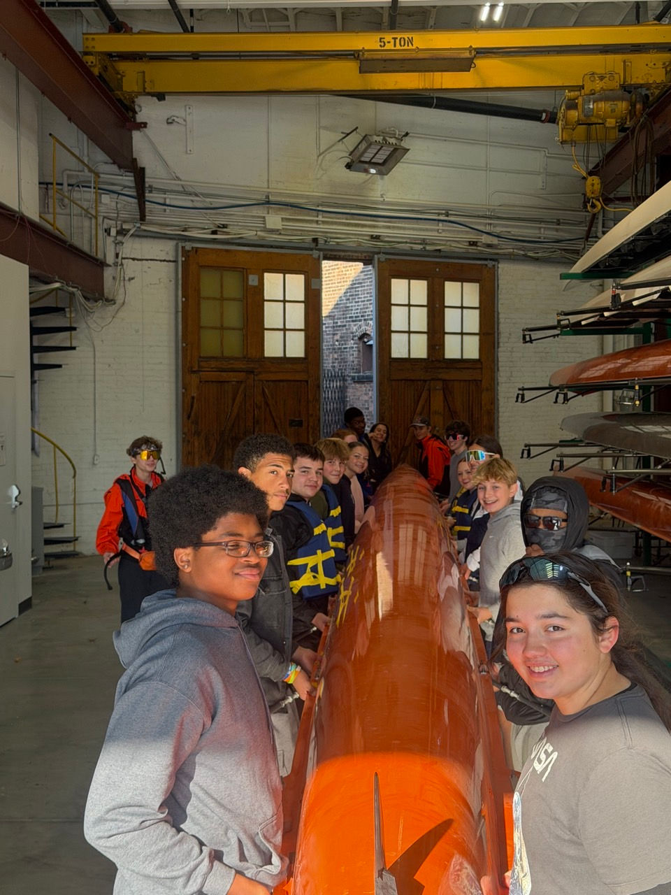 Smiling students in a boathouse with rowing shells