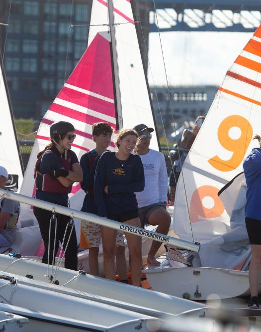 People standing next to small sailboats with orange sails
