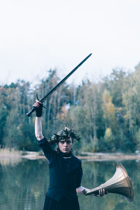 Aramis Freiherr von Maltzahn hält ein Schwert in die Luft. Er steht vor einem Teich