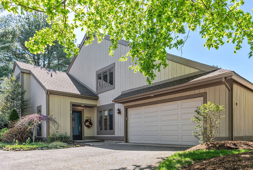 Contemporary house with beige siding, two-story peaked roof, and white garage door. Lush greenery and a tree add a serene, welcoming feel.
