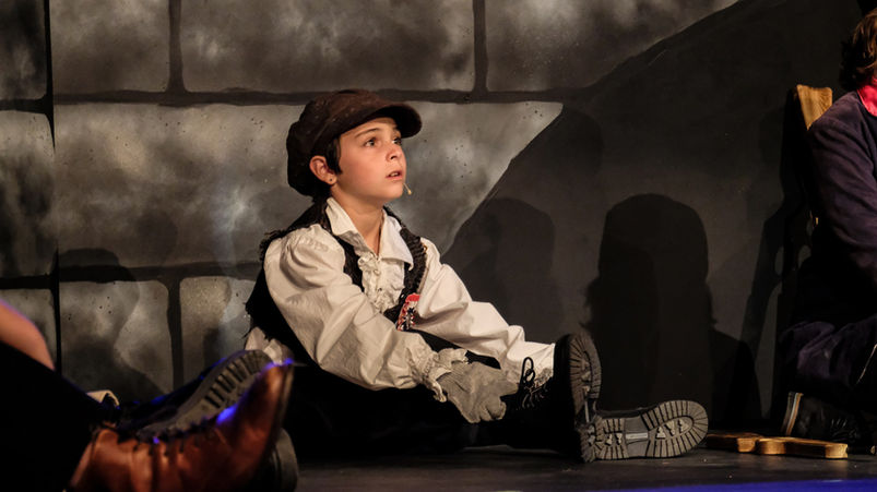 The young student playing "Gavroche" listens to the other student revolutionaries sing. He looks wistful and concerned.
