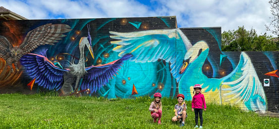 Großflächiges Street-Art-Mural mit Vögeln im Flug auf Außenwand in Grünanlage