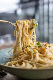 A close-up of creamy spaghetti with herbs and red pepper flakes, twirled on a fork, placed on a light blue bowl, with a blur