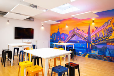 Bright workshop room at werkhain coworking space in Berlin with flexible seating, large screen, acoustic ceiling panels, and colorful wall art for creative sessions and team collaboration.