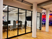 glass-walled conference room with modern lighting and workspace areas visible in the background
