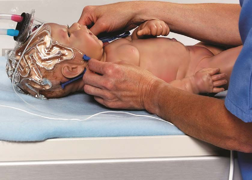 Photograph of a model of a newborn baby undergoing a medical procedure involving brain monitoring, with electrodes attached to a transparent cap on the head and wires connected to medical equipment. Hands of a healthcare professional adjust the setup, highlighting the careful cooling and monitoring of neurological activity in a clinical setting.