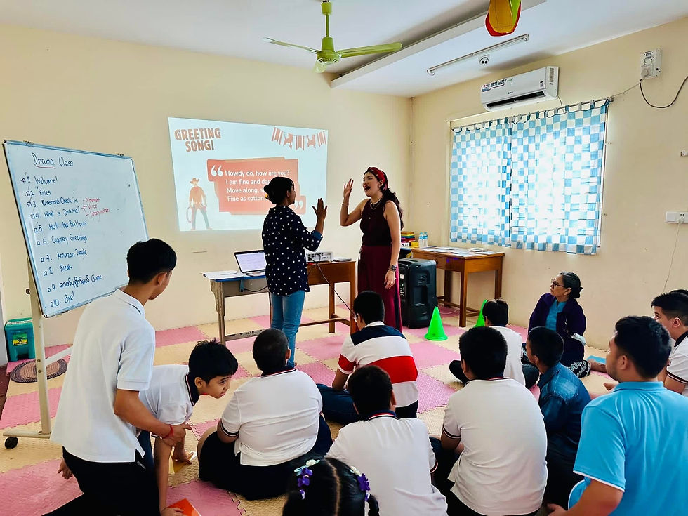 Su demonstrating a drama activity before inviting students with intellectual disabilities to participate. A visual schedule of the lesson is projected and the activities are listed on a whiteboard to support understanding, routine, and independence.