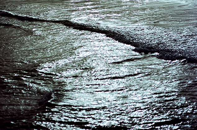 Monochromatic shot of water with sunlight creating highlights in the water, waves visible.
