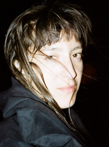 A close-up portrait captures a woman against a dark background. 