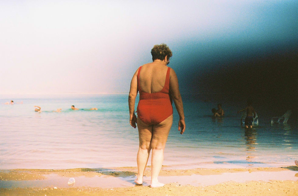 An eye-level shot depicts a woman on a beach, facing away from the viewer, with several other figures in the background.