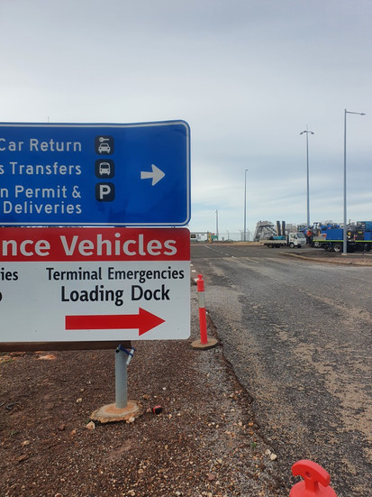 blue sign that says "rental car return, charter bus transfers & eastern permit & terminal deliveries" and below is a green sign that says "Ambulance Vehicles - airfield emergencies Gate Kilo - Terminal Emergencies Loading Dock"