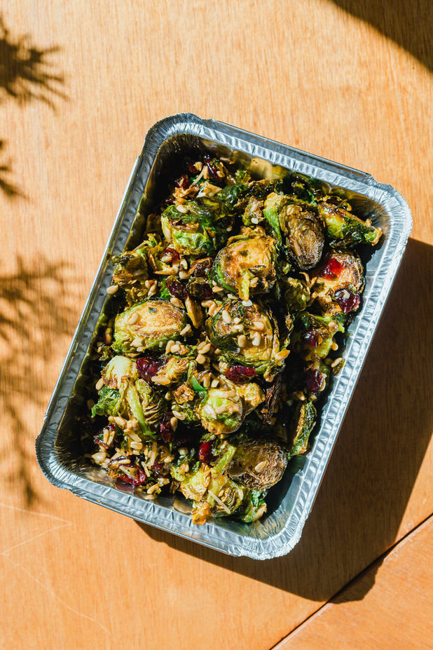 Throwaway metal dish containing roasted Brussels sprouts topped with pine nuts and dried cranberries is ready for a catered event.