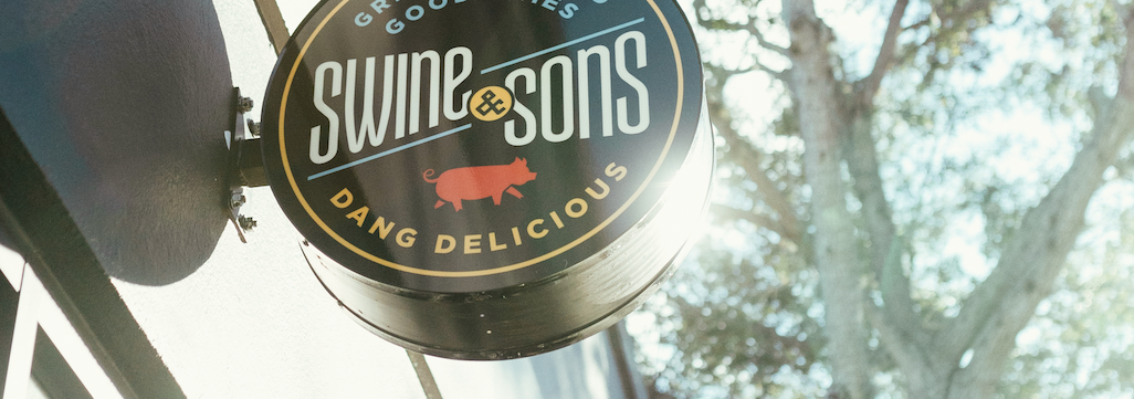 Up close round Swine & Sons logo featuring a pig silhouette sign on the side of a building.
