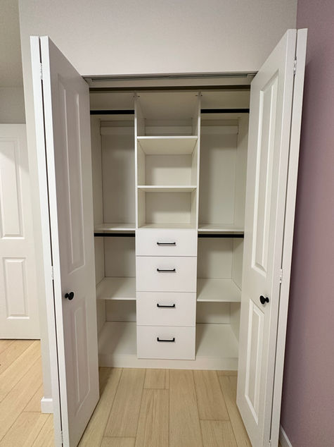 A reach-in closet with double doors, hanging rods, and a center drawer unit.