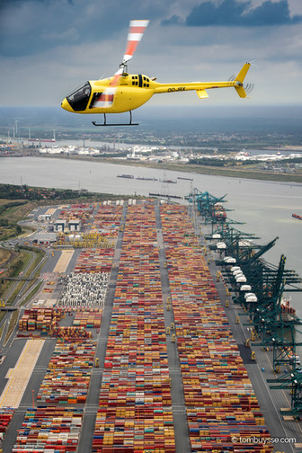 Bell 505 helikopter in vlucht boven de Deurganck Terminal in de haven van Antwerpen tijdens een air-to-air fotoshoot.