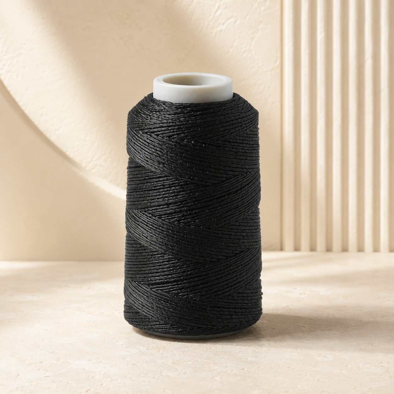 Black Embro 5000m machine embroidery thread cone with white core on a warm textured limestone studio background.