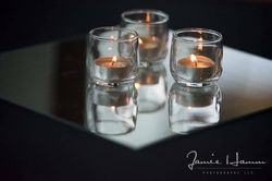 Three shot glasses with lit tea light candles on a reflective surface.