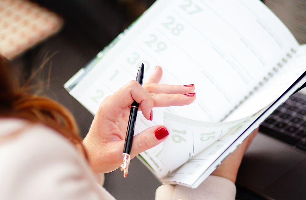 Close-up of a hand with red nails holding a pen over a white calendar planner with green dates, preparing to write