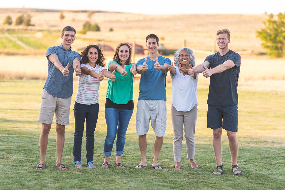 Six individuals are standing with both arms extended in front of them giving the thumbs up sign