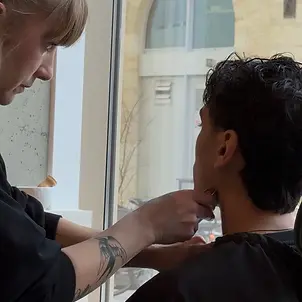 Photo de la coiffeuse-barbière en train de raser la barbe d'un jeune homme.