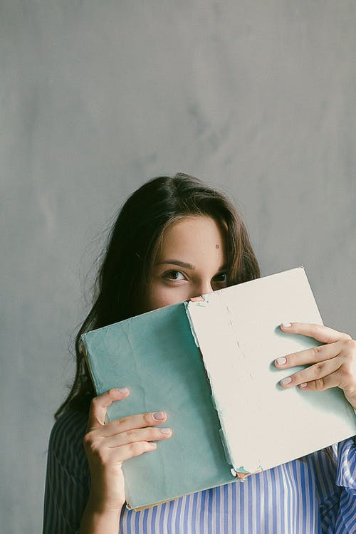 woman hiding part of face behind book