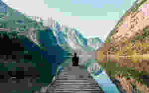 person seated at end of a pier overlooking water and mountains