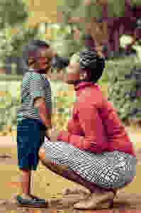 Woman of color squatted down smiling at a young boy of color