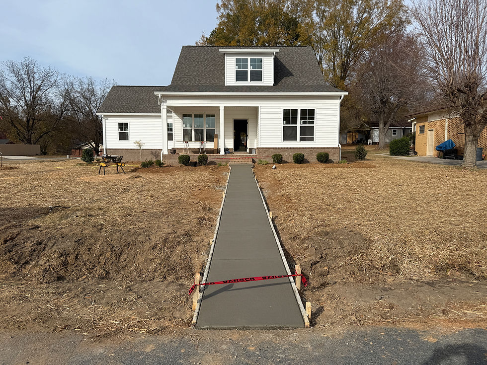 Newly poured straight concrete sidewalk leading to the front porch of a new construction home, showing clean layout and proper grading.