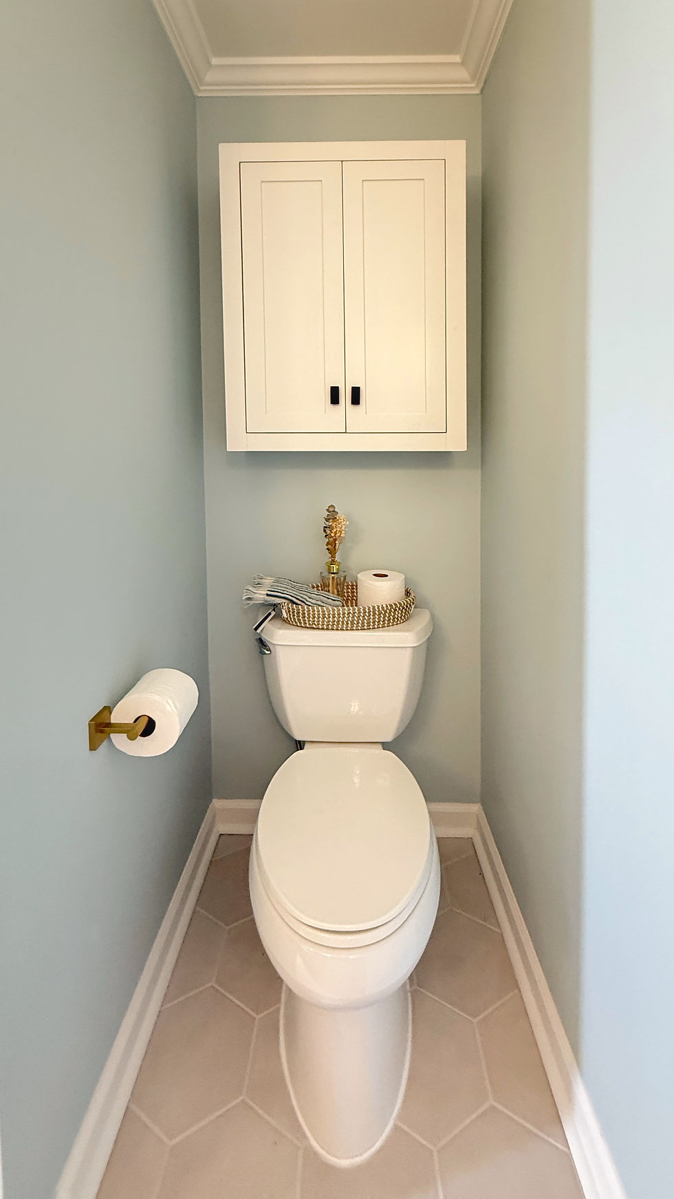 Small bathroom storage solution featuring a wall-mounted cabinet above the toilet for added storage in a timeless light blue and white bathroom design.